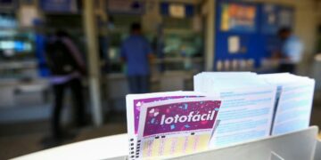Bilhete da Lotofácil em destaque na lotérica, com pessoas ao fundo aguardando atendimento.
