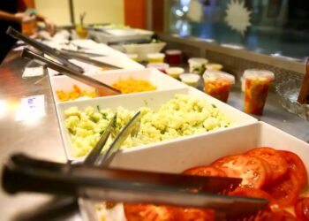 Buffet de saladas com diversos ingredientes frescos, como tomate e cenoura, em recipientes separados.