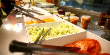 Buffet de saladas com diversos ingredientes frescos, como tomate e cenoura, em recipientes separados.