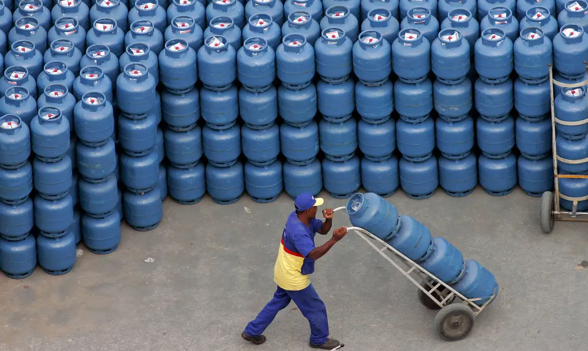 Trabalhador movimentando botijões de gás de cozinha em uma área de distribuição, representando o benefício do Auxílio Gás.