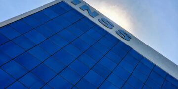 Fachada de prédio com logo do INSS em destaque sob o sol ao fundo.