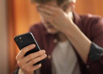 Homem preocupado olhando para o celular, possivelmente vítima de golpe de voz.