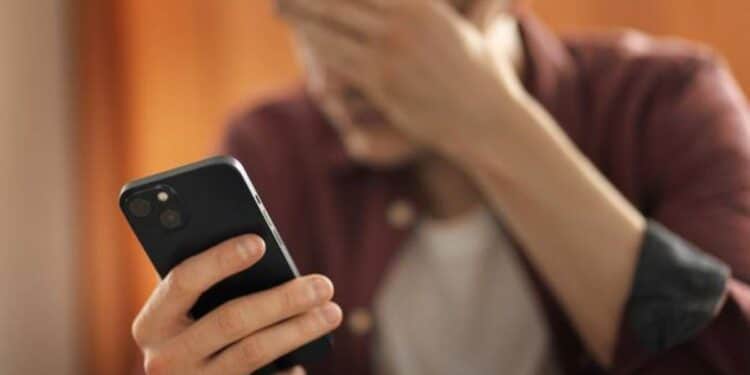 Homem preocupado olhando para o celular, possivelmente vítima de golpe de voz.