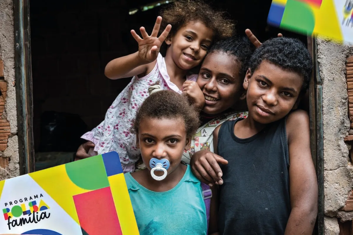 Família beneficiária do Bolsa Família reunida na porta de casa com crianças sorrindo