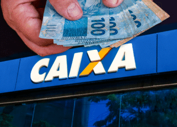 Mãos segurando notas de R$ 100 sobre o logo da CAIXA, simbolizando a liberação do dinheiro do penhor da CAIX.