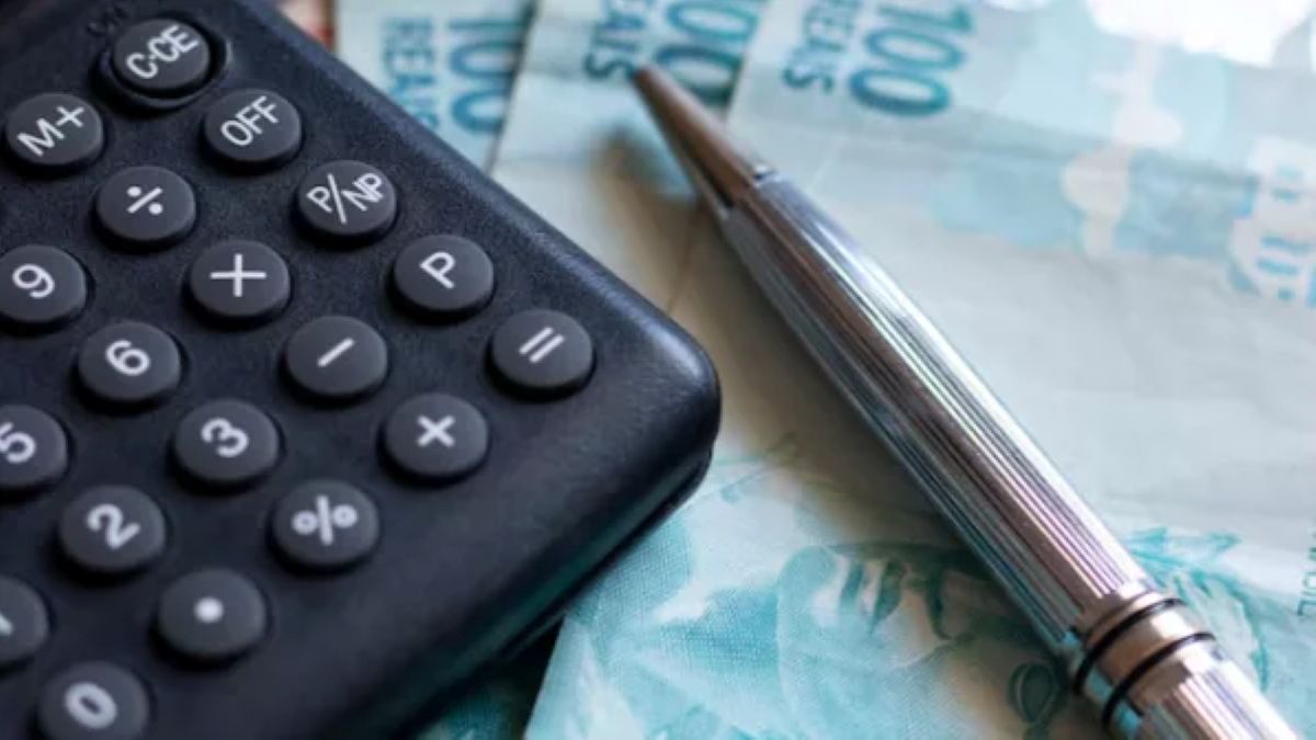 Uma calculadora, uma caneta e notas de 100 reais, simbolizando o cálculo financeiro.