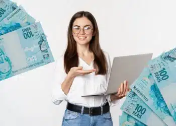 Mulher sorridente com óculos e camiseta branca, segurando um laptop, com notas de 100 reais flutuando ao seu redor.