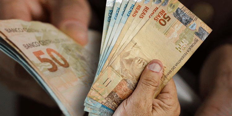 Notas de real sendo contadas por mãos de uma pessoa idosa, representando a carga tributária sobre a população