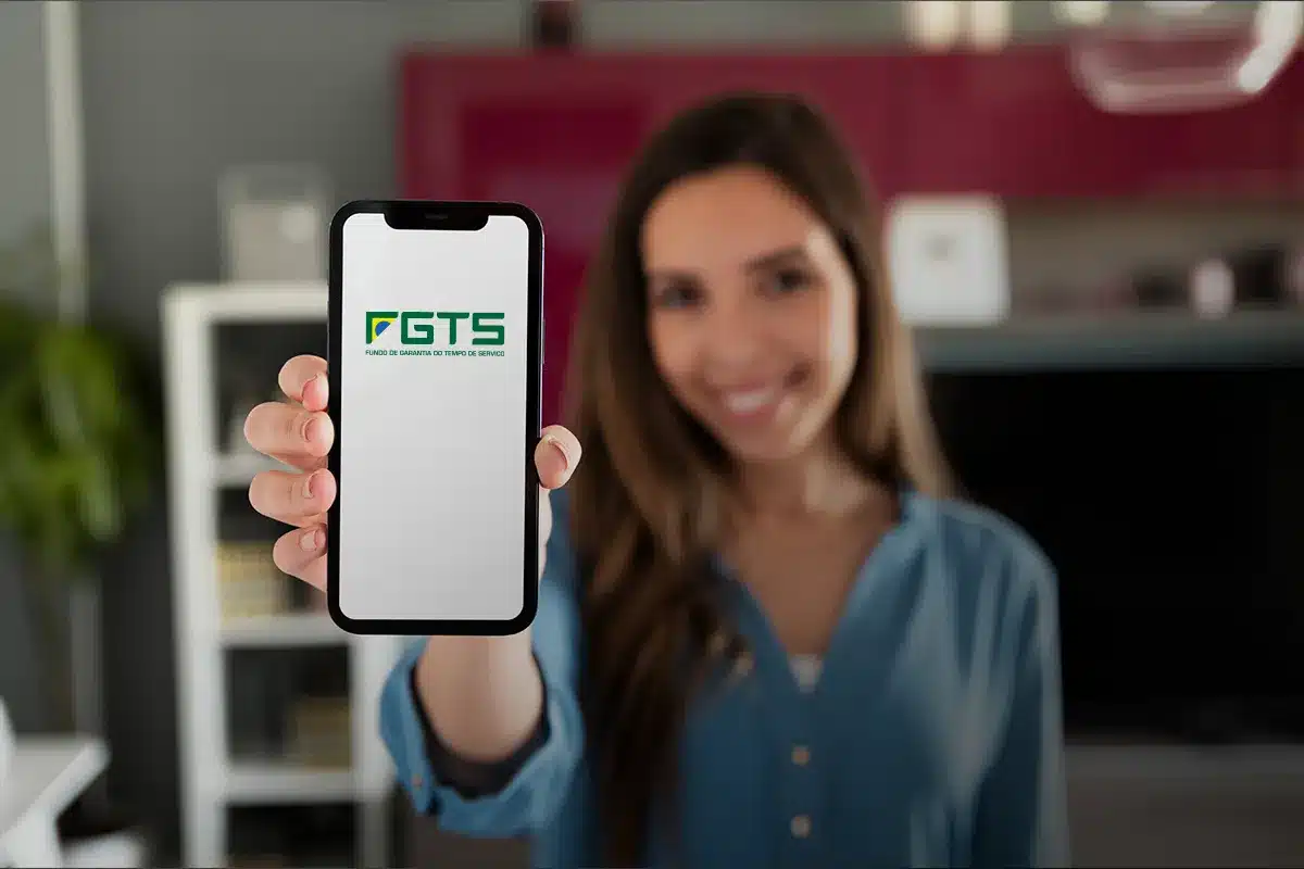 Jovem sorrindo segurando um smartphone que mostra o logo do aplicativo FGTS, simbolizando o saque do fundo.