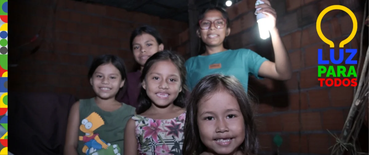 Grupo de crianças sorrindo com uma lâmpada, representando a iniciativa 'Luz para Todos' que leva energia elétrica a comunidades rurais e isoladas na Amazônia Legal.