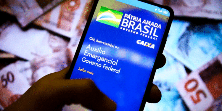 Tela de celular mostrando aplicativo do Auxílio Emergencial do Governo Federal, com fundo de cédulas de reais desfocadas.