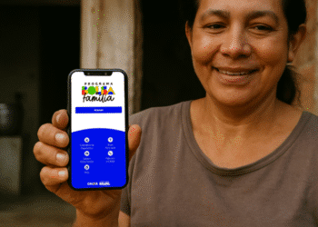 Mulher sorridente segura celular com aplicativo do Bolsa Família aberto na tela.
