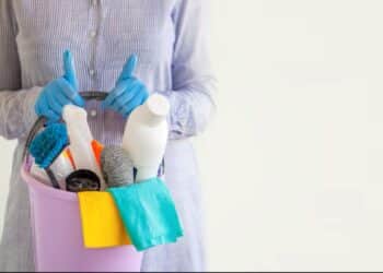 Mulher de luvas azuis segurando um balde de limpeza com produtos e vassouras, referenciando as empregadas domésticas.