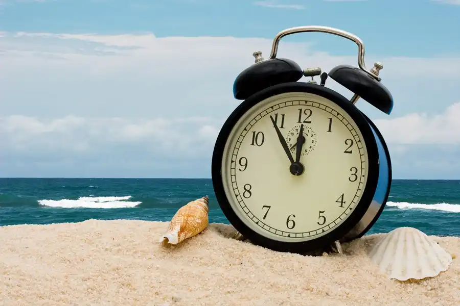 Relógio de alarme em uma praia, com o mar ao fundo, simbolizando o debate sobre o horário de verão.