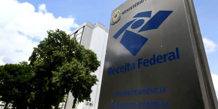 Placa da Receita Federal do Brasil sob céu azul com nuvens e árvores, simbolizando a instituição fiscal.