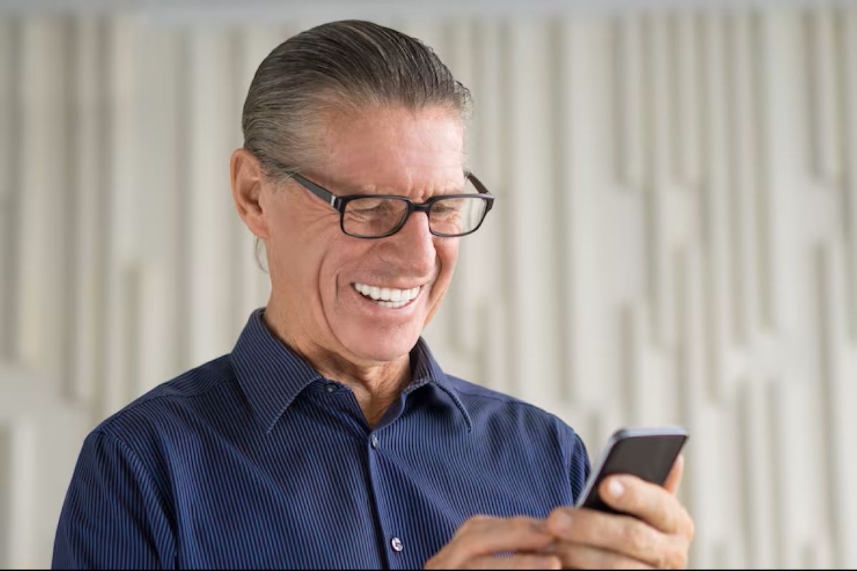 Aposentado sorridente usando celular para fazer consulta de valores do INSS