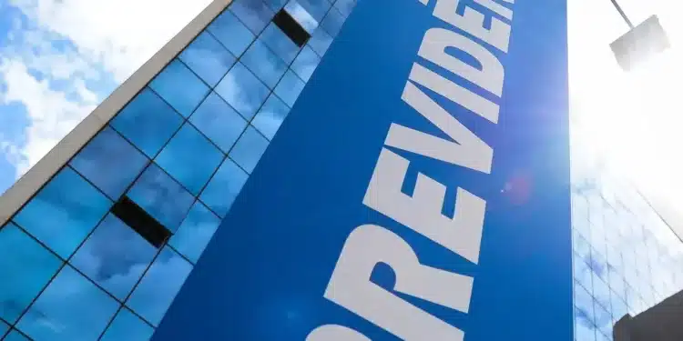 Painel de vidro refletindo o céu e a inscrição 'PREVIDÊNCIA' em uma fachada de edifício, destacando uma nova proposta para aposentadoria antes dos 50 anos.