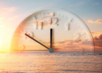 Imagem de um relógio se sobrepondo a uma paisagem de mar ao entardecer, simbolizando a expectativa do retorno do horário de verão no Brasil.