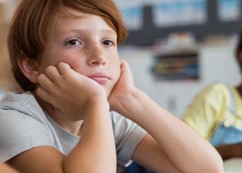 Criança com expressão pensativa em sala de aula, possivelmente enfrentando dificuldades de atenção.