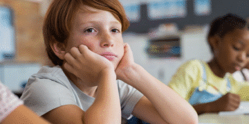 Criança com expressão pensativa em sala de aula, possivelmente enfrentando dificuldades de atenção.