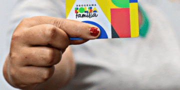 Foto de uma mão segurando um cartão do Programa Bolsa Família com fundo colorido.