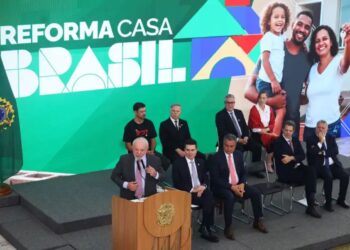 Presidente discursando no lançamento do programa 'Reforma Casa Brasil', com um telão exibindo famílias felizes e autoridades presentes.
