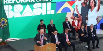 Presidente discursando no lançamento do programa 'Reforma Casa Brasil', com um telão exibindo famílias felizes e autoridades presentes.