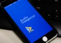 Tela de smartphone mostrando o aplicativo Auxílio Emergencial com fundo azul e símbolo amarelo