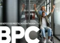 Pessoa com deficiência cadeirante comemorando ao lado de uma mulher enquanto segura um folheto do BPC. Início do pagamento do Benefício de Prestação Continuada INSS em Outubro.