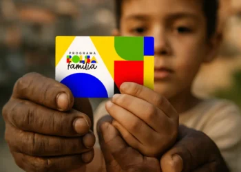 Cartão do Programa Bolsa Família segurado por mãos de adulto e criança ao fundo desfocado