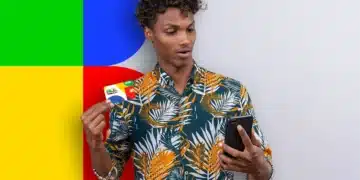 Homem jovem surpreso segurando o cartão do Bolsa Família e olhando para o celular, com um fundo abstrato nas cores da bandeira do Brasil.