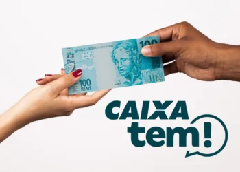 Mãos segurando uma nota de 100 reais com logo do app Caixa Tem ao fundo
