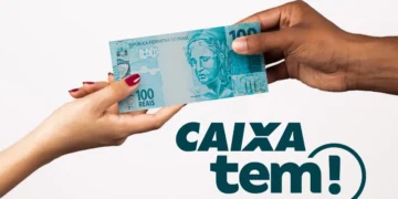 Mãos segurando uma nota de 100 reais com logo do app Caixa Tem ao fundo
