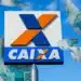 Logotipo da Caixa Econômica Federal em destaque, com notas de R$ 100 flutuando ao redor em um céu azul, simbolizando a liberação de dinheiro e benefícios financeiros.