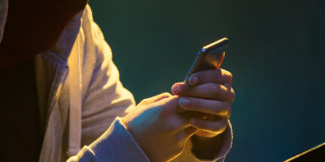 Pessoa usando um smartphone em ambiente escuro, com parte do rosto coberta, simbolizando fraude ou uso indevido de informações em golpes online.