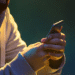 Pessoa usando um smartphone em ambiente escuro, com parte do rosto coberta, simbolizando fraude ou uso indevido de informações em golpes online.