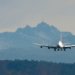 Avião comercial de grande porte aterrissando com montanhas e floresta ao fundo, simbolizando viagem aérea