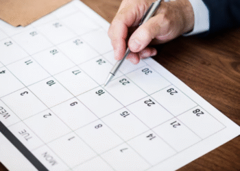 Mão de uma pessoa marcando datas em um calendário genérico, simbolizando o planejamento de feriados e datas comemorativas de novembro de 2025.