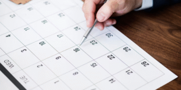 Mão de uma pessoa marcando datas em um calendário genérico, simbolizando o planejamento de feriados e datas comemorativas de novembro de 2025.