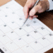 Mão de uma pessoa marcando datas em um calendário genérico, simbolizando o planejamento de feriados e datas comemorativas de novembro de 2025.