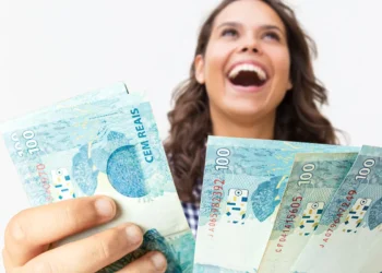 Jovem sorrindo e segurando notas de R$ 100, simbolizando a conquista financeira e o planejamento bem-sucedido para a aposentadoria.