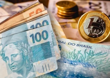 Dinheiro em espécie com notas de 100 e 50 reais e moedas de real amareladas em fundo desfocado