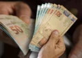 Mãos segurando e contando cédulas de Real brasileiro, notas de 50 e 10 reais visíveis