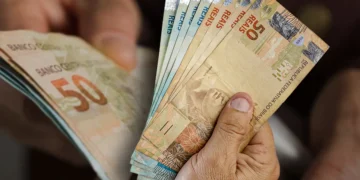Mão segurando várias cédulas de real em diferentes valores, incluindo notas de 50 reais