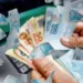 Cédulas de real sendo contadas, representando o 13º salário de 2025 e seus descontos e prazos.