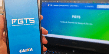Imagem de uma mão segurando um smartphone com o aplicativo FGTS da Caixa aberto, ao lado de um laptop exibindo o site do FGTS em fundo gradiente azul e verde.