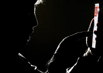 Silhueta de homem interagindo com smartphone iluminado em fundo preto escuro