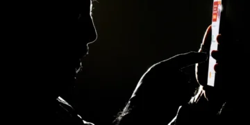 Silhueta de homem interagindo com smartphone iluminado em fundo preto escuro