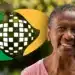 Mulher idosa sorridente usando camiseta rosa com símbolo colorido de milho ao fundo desfocado