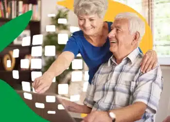 Casal de idosos sorrindo e usando notebook em ambiente iluminado e acolhedor